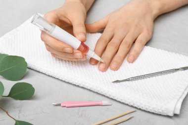 Tırnaklara, havluya ve okaliptüs dalına gri grunge arka planda tırnak yağı süren kadın eller.