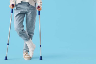 Mavi arka planda koltuk değnekleriyle kazadan sonra yaralanan genç kadın.