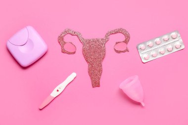 Pembe arka planda haplı kağıt rahim, regl kupası ve hamilelik testi.