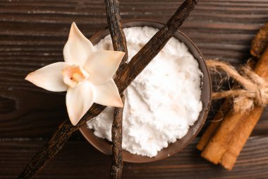 Bir kase vanilya tozu, sopa ve çiçek koyu ahşap arka planda, yakın plan.