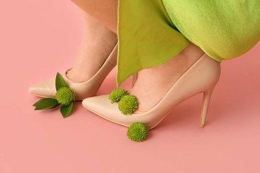 Pembe arka planda kasımpatı çiçekleri olan yüksek topuklu güzel genç bayanların bacakları.