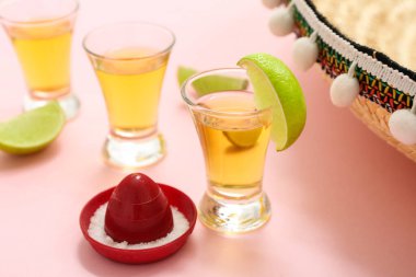 Pembe arka planda tekila ve limon dilimleri, yakın plan.