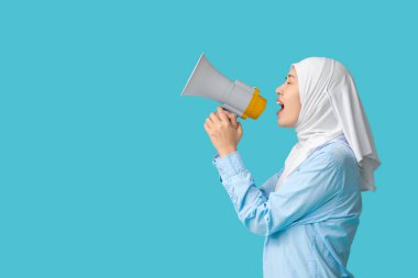 Genç Asyalı Müslüman kadın mavi arka planda megafona bağırıyor. Ulusal Duyulma Günü