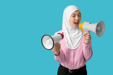 Genç Asyalı Müslüman kadın mavi arka planda megafonlara bağırıyor. Ulusal Duyulma Günü