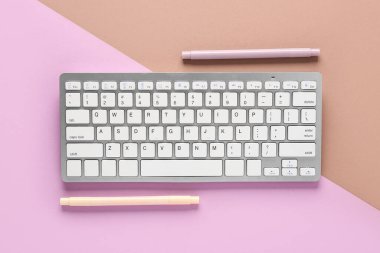 Gri bilgisayar klavyesi ve kahverengi eflatun kaplamalı keçeli kalemler. Üst görünüm