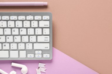 Gri bilgisayar klavyesi, keçeli kalem ve kahverengi eflatun arka planda kulaklık. Üst görünüm