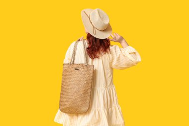 Sarı arka planda şık hasır çantalı, güzel genç bir kadın.