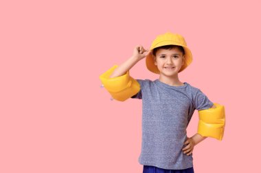 Panama şapkalı şirin bir çocuk ve pembe arka planda şişme kolluklar.