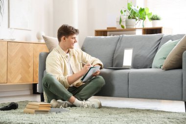 Erkek öğrenci evde çevrimiçi öğretmenle çalışırken not alıyor