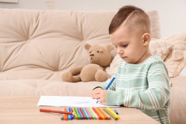 Evdeki masada keçeli kalemle çizen küçük çocuk.