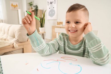 Evdeki masada keçeli kalemle çizen komik küçük çocuk.