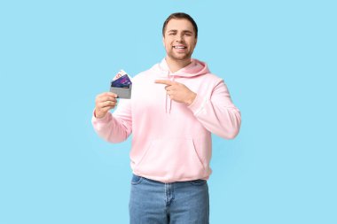 Mutlu genç adam mavi arka planda kredi kartlarıyla cüzdanını gösteriyor.