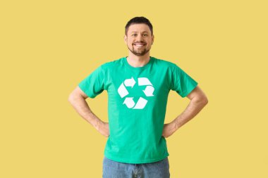 Sarı arka planda geri dönüşüm logosu olan tişörtlü mutlu genç adam. Ekoloji kavramı