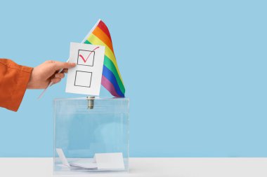 Mavi arka planda oy sandığının yanında LGBT bayrağı taşıyan kadın