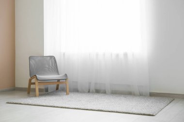 Odadaki ışık perdesinin yanındaki sandalye ve halı.