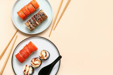 Lezzetli suşi ruloları, bej arka planda kaşık ve çubuklar olan tabaklar.