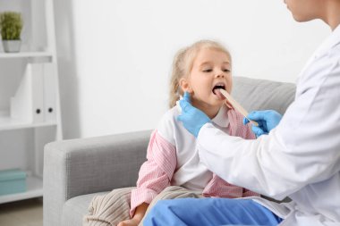 Pediatrician examining little girl with tongue depressor in clinic