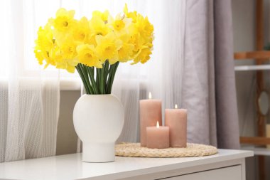 Masası, mumları ve narsisli çiçekleri olan şık bir oda.