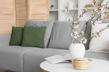 Modern oturma odasındaki sehpanın üzerinde çiçek açan dallar, şarjör ve kale sepetleri olan bir vazo.