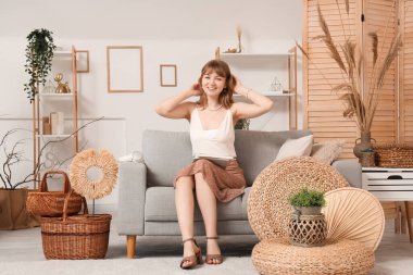 Genç, güzel bir kadın, oturma odasında, kanepede oturuyor.