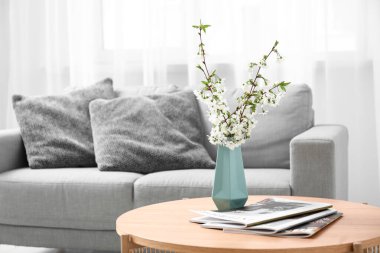 Şık oturma odasındaki masanın üzerinde çiçek açan dalları olan mavi vazo.