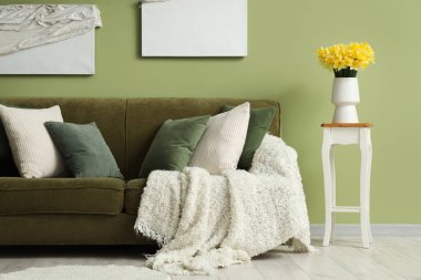 Oturma odasının içinde yeşil kanepe ve masadaki vazolarda nergisler.