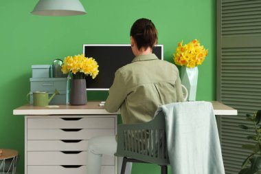 Ofiste masa başında çalışan nergis ve bilgisayarlı genç bir kadın.