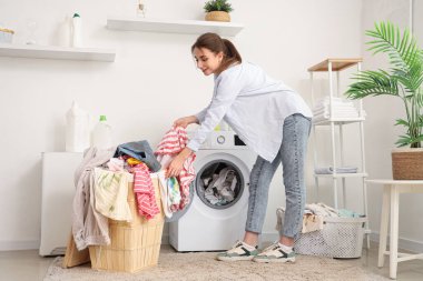 Kirli çamaşırları evdeki çamaşır makinesine koyan genç bir kadın.