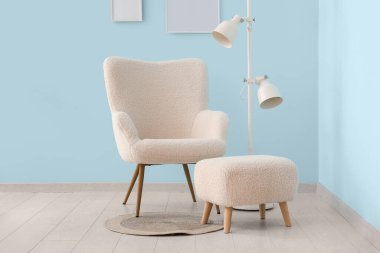 Mavi duvarın yanında beyaz koltuk, lamba ve puf.