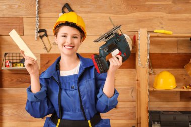 Kablosuz yapbozu ve atölyede tahta kalası olan genç bir kadın marangoz. İşçi Bayramı kutlamaları