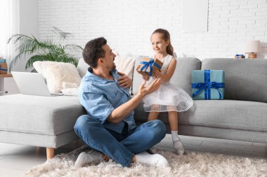 Küçük kız, oturma odasında babasına hediye veriyor. Babalar günü kutlaması.