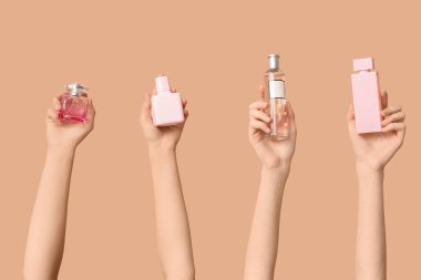 Kahverengi arka planda farklı parfüm şişeleri olan kadın elleri.