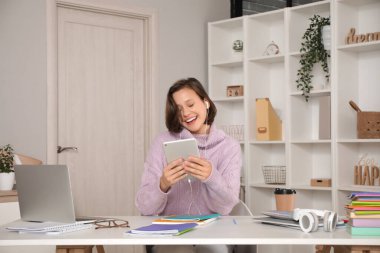 Kulaklıklı güzel bir öğrenci evde tablet bilgisayarla çalışıyor.