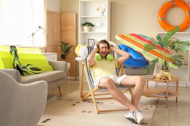 Kulaklıklı bir erkek turist tatilde güverte sandalyesinde oturuyor.