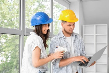 Dizüstü bilgisayarı olan bir erkek müteahhit ve odada tamir planlaması yapıyor.