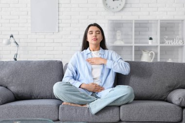 Beautiful young woman doing breath practice on sofa at home