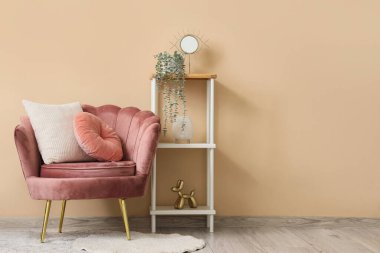 Yastıklı koltuk, dekorasyonlu raf ünitesi ve oturma odasındaki bej duvarın yanına bitki.