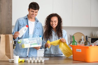 Mutfakta çöp konteynırları ve çöp torbaları olan genç bir çift.