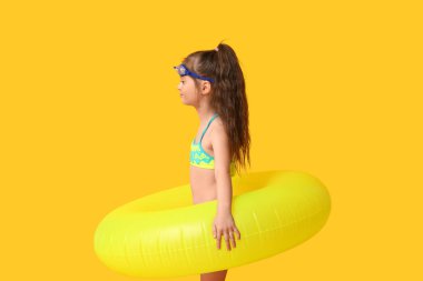 Yüzme gözlüklü ve sarı arka planda şişme yüzüklü şirin bir kız.