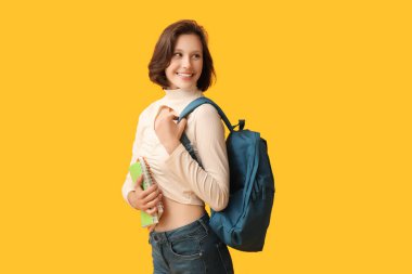 Sarı arka planda not defterleri ve sırt çantasıyla güzel bir kız öğrenci.