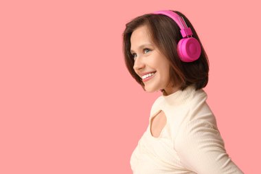 Pembe arka planda modern kulaklıklı mutlu genç kadın.