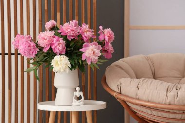 Kahve masasında şakayık çiçekli vazo, koltukta ve odada puf.