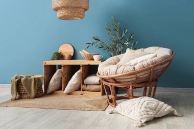 Yastıklı koltuk, raf ünitesi, dekoratif zeytin ağacı ve oturma odasının içinde ekoseli sepet.