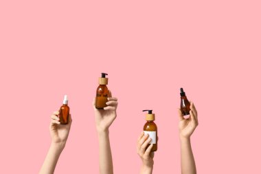 Pembe arka planda kozmetik ürünleri olan kadın elleri