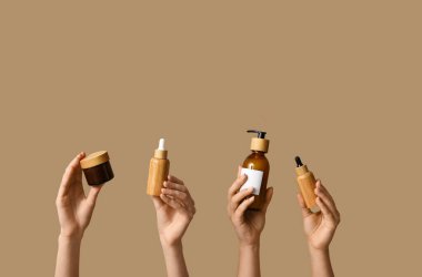 Bej arka planda şişe ve kozmetik ürünlerle dolu kadın elleri