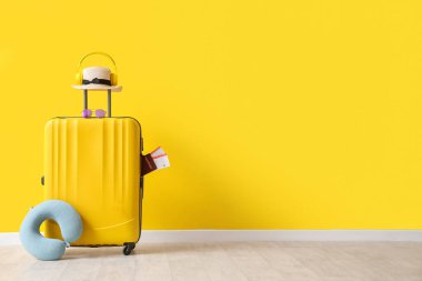 Sarı duvarın yanında boyun yastığı, şapka ve pasaport dolu bavullar.