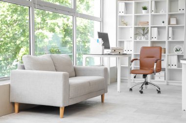 Çalışma yeri, raf ünitesi ve beyaz kanepesi olan açık bir uzay ofisi.