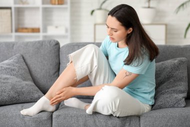 Evdeki kanepede bileğindeki ağrıdan muzdarip genç bir kadın.