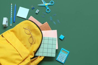 Yeşil arka planda farklı kırtasiye malzemeleri ve gözlüklerle modern okul sırt çantası.