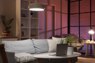 Sofra, modern dizüstü bilgisayarlı masa ve oturma odasının içinde parlayan lambalar.